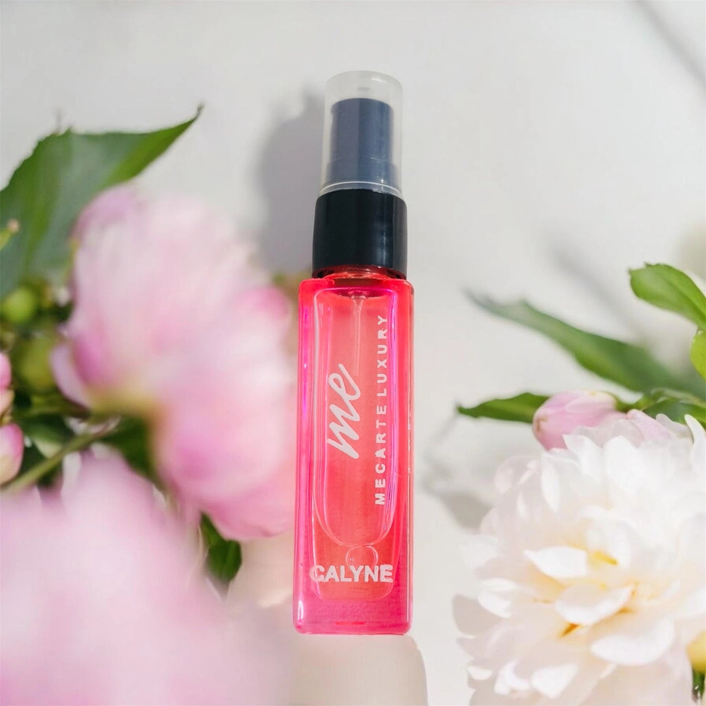 Travel size perfume Calyne Mini Perfume 8ml bottle surrounded by soft pink flowers.