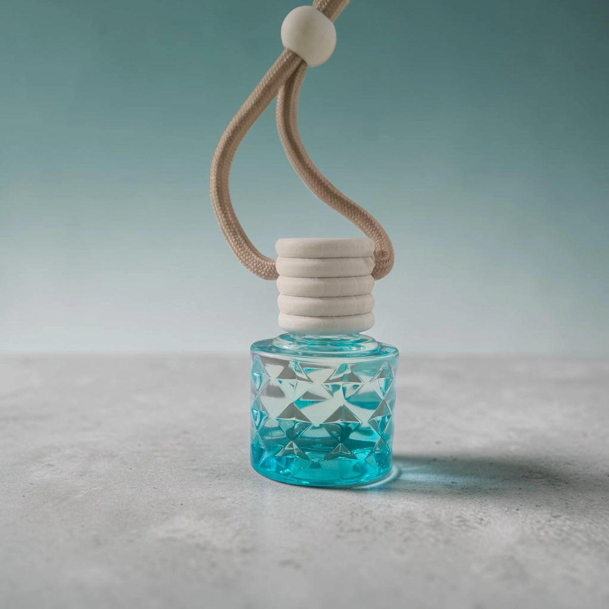 ME HHH Gold car perfume bottle with blue liquid and beige hanging cord, highlighted against a soft gradient background.